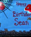 Spiderman 4th Birthday Cake. Blue buttercream iced, sheet cake decorated with spiderman spinning his web over the city. 