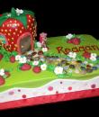 Strawberry Shortcake Birthday Cake,  Green buttercream iced, sheet cake decorated with strawberry shaped house, cobblestone sidewalk path, strawberries, flowers, and a plastic strawberry shortcake doll.  Everything on this cake is EDIBLE.  (Plastic character figurine was provided by client). (Serves 12-90 party slices)
